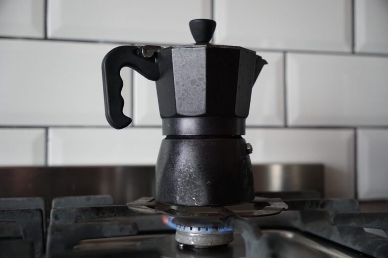 Schwarze Espressokanne auf der Gasflamme vor weißen Fliesen